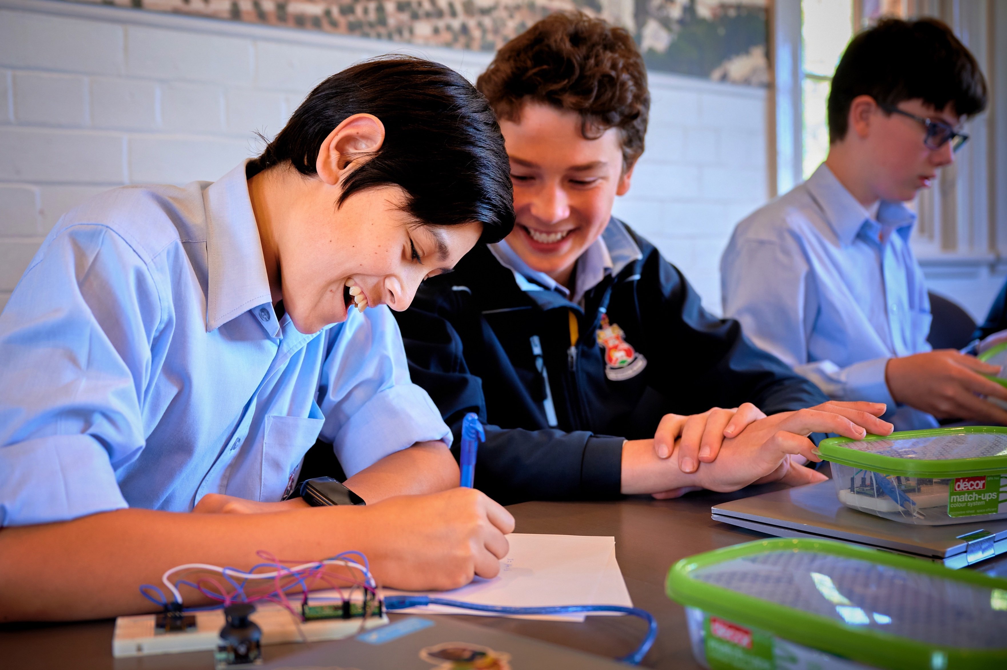 Picture of students interacting with electronics components, pen, and paper.